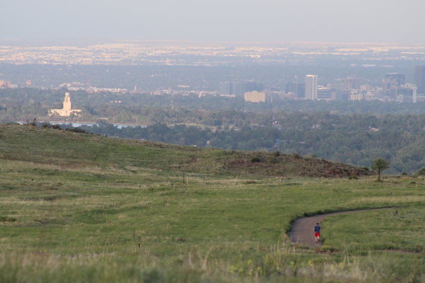 A runner, bottom right, runs along South Table Mountain's Old Quarry Trail as the sun sets on Lakewood and downtown Denver, background, on June 16.